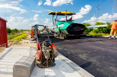 Vibrating plate machine for compacting tarmac parked on the unfinished bridge. Spreader machine lays, pours hot asphalt