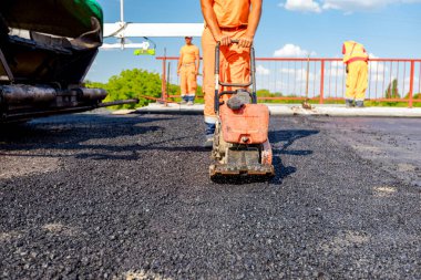 View on worker who is compacting asphalt with vibration plate, compactor machine on the bridge under construction.
