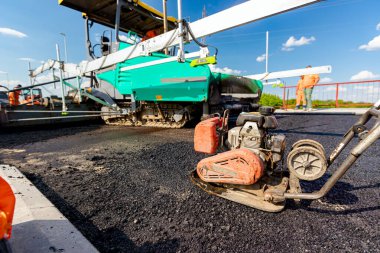 View on worker who is compacting asphalt with vibration plate, compactor machine on the bridge under construction.