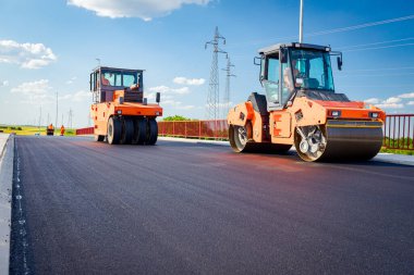 Several steamrollers that are flatting fresh asphalt, spreading layer of hot tarmac on prepared ground at the bridge under construction.