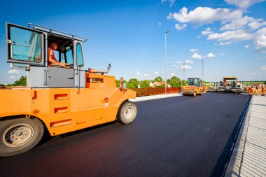 Several steamrollers that are flatting fresh asphalt, spreading layer of hot tarmac on prepared ground at the bridge under construction.