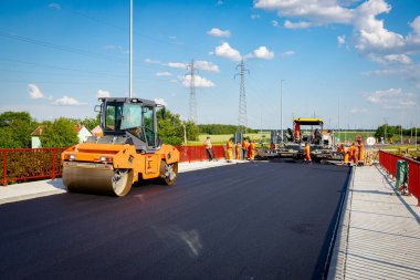 Several steamrollers that are flatting fresh asphalt, spreading layer of hot tarmac on prepared ground at the bridge under construction.