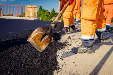 Çok az işçi kürek kullanıyor, düzgün ölçülerde taze asfalt katmanı kuruyor ve sıcak asfalt döküyor..