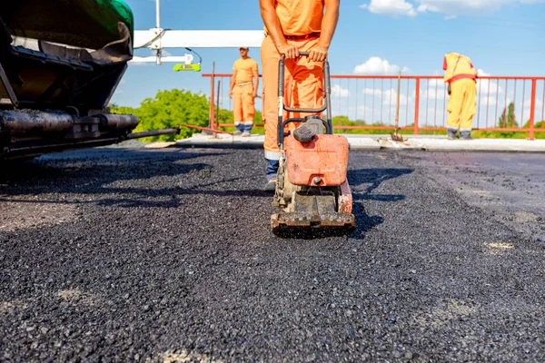 View on worker who is compacting asphalt with vibration plate, compactor machine on the bridge under construction.