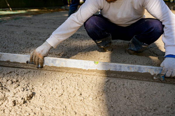 Строитель носит перчатки, как выравнивание свежего бетона с металлической пластины после заливки. 