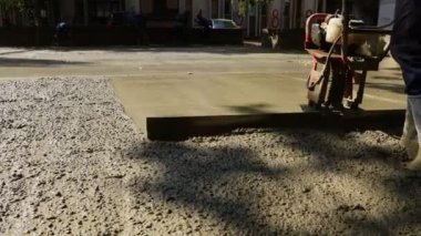 İnşaat işçisi, dökme sonrası çimentoyu hizalamak ve sıkıştırmak için yeni betonu motorlu elektrikli aletle, titreşimli metalle düzleştiriyor.. 