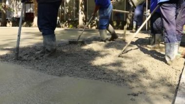 Construction workers, riggers are using rake to spreading, leveling concrete covering square reinforcement, pouring layer of concrete in foundation.