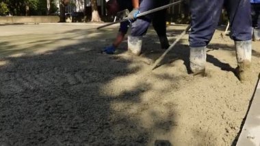 Construction workers, riggers are using rake to spreading, leveling concrete covering square reinforcement, pouring layer of concrete in foundation.