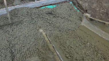 Unloading fresh concrete, pouring layer of concrete flow  over ramp covering square reinforcement on plastic foil. Construction worker is using rake to spreading, leveling fresh cement