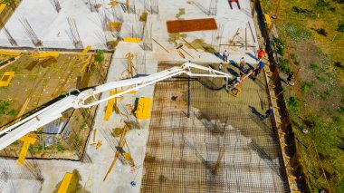 Aerial view construction worker is directing the pump tube as pouring layer of concrete in building foundation. Worker is using power tool, compactor, electric vibratory, compacting fresh concrete.