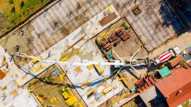Aerial top view construction site, mixer truck pouring concrete into pump machine, pumping out, worker directing on right direction, building foundation. Riggers, workers leveling concrete