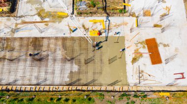 Aerial top view construction worker is directing the pump tube on right direction, pouring layer of concrete in building foundation. 
