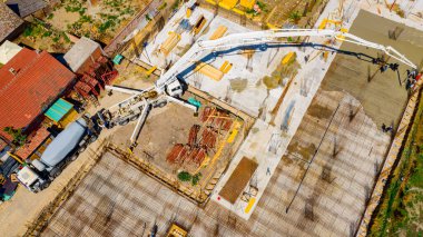 Aerial view construction site, mixer truck pouring concrete into pump machine, pumping to exit tube, worker is directing on right direction, building foundation. Riggers, workers leveling concrete