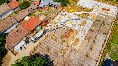 Aerial view construction site, mixer truck pouring concrete into pump machine, pumping to exit tube, worker is directing on right direction, building foundation. Riggers, workers leveling concrete