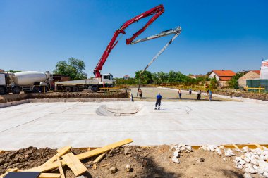 Construction site, mixer truck pouring concrete into pump machine pumping to exit tube, worker directs it on the right direction, building foundation. Riggers, workers leveling concrete