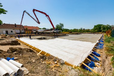 Construction site, mixer truck pouring fresh concrete into pump machine pumping to exit tube, worker directs it on the right direction, building foundation. Riggers, workers leveling concrete