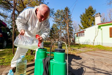 Çiftçi, meyve ağaçlarını mantar veya haşarat hastalıklarından korumak için meyve suyu püskürtmek için plastik sırt çantasındaki böcek ilacının su ve botanik çözeltilerini hazırlıyor..