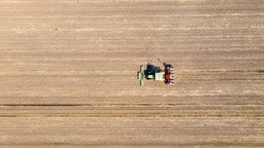 Üstten bakıldığında, traktörün tarla, toprak, yeni tahıl, mısır, mısır ekimi üzerine mekanik tohum ekme makinesi çekmesi..