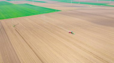 Manzaranın üstünde, ekilebilir tarla, toprak, yeni tahıl, mısır, mısır ekimi üzerine mekanik tohum ekme makinesi çeken bir traktör var..