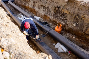 Zrenjanin, Voyvodina, Sırbistan - 21 Ekim 2022: Rigger, izole edilmiş boru hattına iki kaynaşmış izole borunun üzerinde erimek üzere gaz üfleme borusu meşalesi kullanarak termal koruma tabakasını yapıştırıyor.