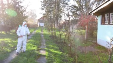 Koruyucu giysili çiftçi ve koruyucu tıbbi cerrahi yüz maskesi ile meyve ağaçlarını uzun spreyle ilaçlarken, ilkbahar başında mantar hastalıklarından veya haşaratlardan korunurken,