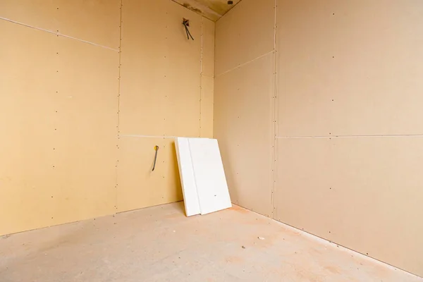 A few pieces of plaster boards are waiting to be installed on the partition walls of building under construction. Exposed one electrical socket with the top cover removed