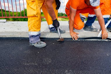 Workers attach a bitumen black tape to protect the roadside of bridge from water. Waterproofing material designed to resist and prevent water from passing through the joint placed on the pavement