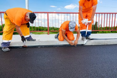 Workers attach a bitumen black tape to protect the roadside of bridge from water. Waterproofing material designed to resist and prevent water from passing through the joint placed on the pavement