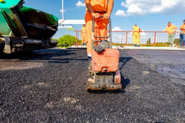 View on worker who is compacting asphalt with vibration plate, compactor machine on the bridge under construction.