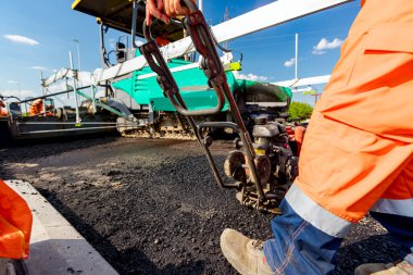 View on worker who is compacting asphalt with vibration plate, compactor machine on the bridge under construction.
