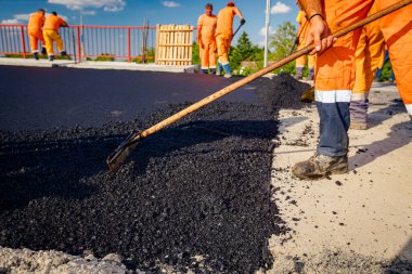 Çok az işçi kürek kullanıyor, düzgün ölçülerde taze asfalt katmanı kuruyor ve sıcak asfalt döküyor..