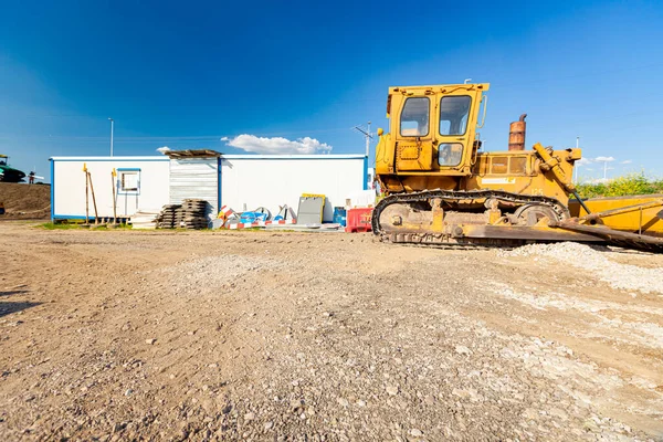 Industrial yellow earthmover parked at the construction site in front of mobile container office for the site manager and employees.