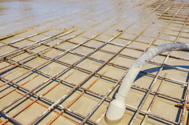 Taze sıvı betonu sıkıştırmak için kullanılan elektrikli titreşim aleti, sıkıştırıcı, yeni binanın temeli olan kare güçlendirmenin arasına yerleştirilir..