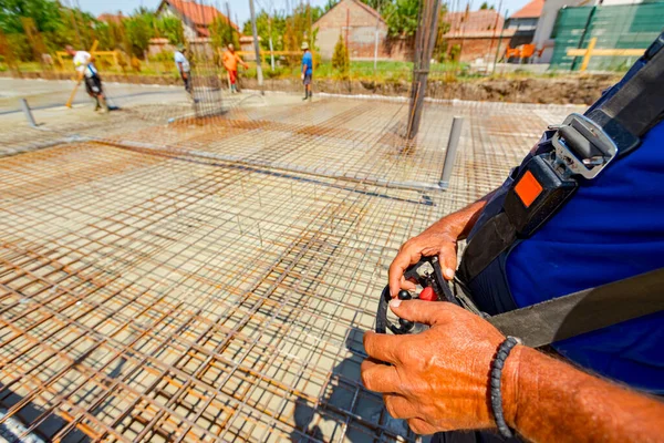 Operator, worker is holding industrial remote, wireless, console control with joystick to directing pump tube on right direction, pouring layer of concrete in building foundation, construction site.