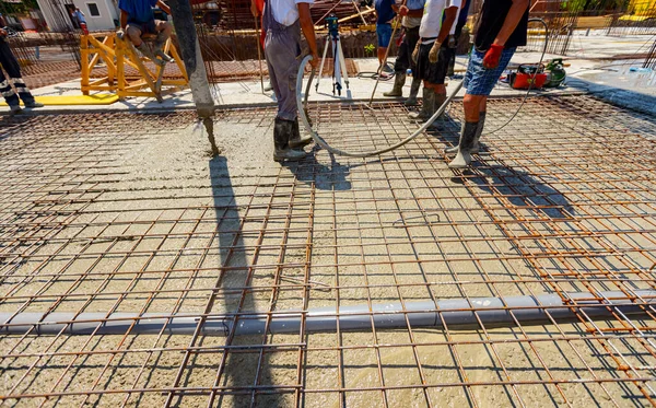 Worker is using vibration power tool, compactor, for compacting fresh liquid concrete, flowing slowly among square reinforcement in the base of new building