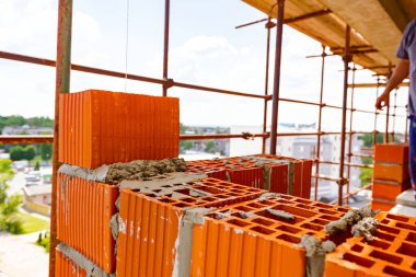 Duvarın kenarı kırmızı bloklardan ve harçtan yapılmış. Arka planda paslı yapı iskelesi var..