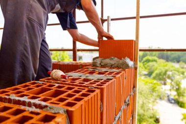 Kırmızı bloklara yerleştirilmiş bir makara dolusu tel. İşçilere yeni yapılarda düz mesafeler oluşturmada yardımcı olmak için araç, arka planda duvar örmek için kırmızı bloklar kullanır. 