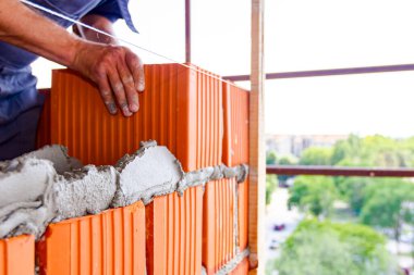 Mason, tuğla ustası düz olması için tel hattının yanına duvar örüyor..