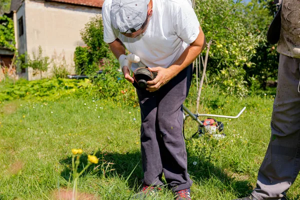 包帯傷手修理トリマーと修理工は 果樹園や桃の草を刈るためのトリマーヘッドコイルの文字列を調整します 庭道具の整備 — ストック写真