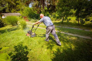 Bahçıvan bahçesinde çim biçme makinesiyle meyve ağaçları arasında çim biçiyor..