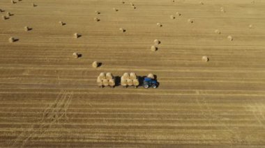 Kamera panelinin üstünde, doli yan hareket ediyor, traktör tarla, tarla, buğday sakalı ve tarla arazisi üzerinde saman dolu yuvarlak balyalarla dolu..