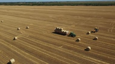 Dolly, kazıcının etrafındaki yörüngeyi tarladaki saman balyalarını, forklift bıçağı ve ilave taşıyıcı bıçak kullanarak traktörle tarlaya yüklerken hareket ettiriyor..