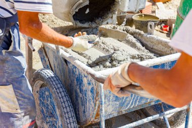 Ekip çalışması, işçiler havan topu karıştırma makinesinden el arabasına taze havan topu döküyorlar. İnşaat alanı çalışıyor
