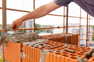 İşçi, duvar ve tuğla ustası yapmak için kırmızı bloklara havan topu sürmek için spatula, mala kullanıyor. Bina yapım aşamasında..