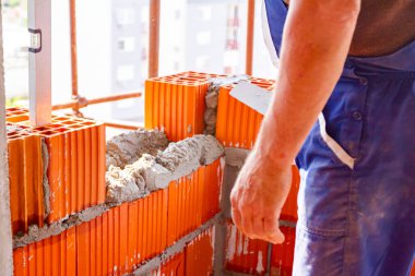 Kırmızı seramik blokta sıkışan kontrol ölçümü için ruh seviyesi, duvar ustası inşaat halindeki bina duvarını örmek için tuğla kullanıyor..