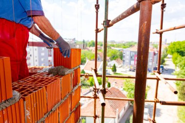 İnşaatçı kırmızı bloklardan yapılmış yeni kırmızı tuğla duvarları kontrol etmek için ruh seviyesini kullanıyor, tuğlacı. İnşaat halindeki yapının kenarına.