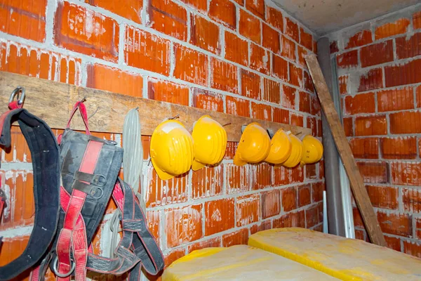 労働者の産業用作業用具 黄色のヘルメットと安全ベルトは 赤いレンガの壁に取り付けられた木製の板と釘で作られた仮設ハンガーにかかっています — ストック写真