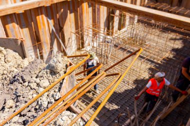 Seçilmiş paslı çelik bükülmüş destek çubukları inşaat alanına yerleştirilmeye hazır. Hendekte, işçiler metal yığınlarıyla çevrili köprü temeli için armatür çubukları kuruyor..