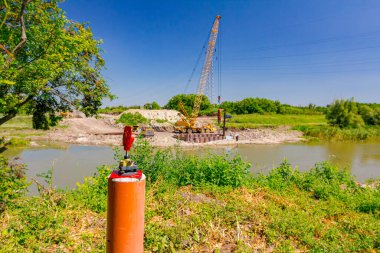 Kırmızı metal direkteki dengeleyici cihazın bir kısmı, inşaat halindeki köprüdeki noktaların kesin olarak saptanmasını sağlıyor. Nehrin karşısında eski seyyar vinç var..