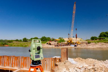 Elektronik seviyelendirme cihazı büyük inşaat projelerine girişmeden önce hassas ölçümler yapılmasını sağlar. Köprü temeli için nehir boyunca metal yığınları pnömatik çekiçle taşınabilir vinçtir..        